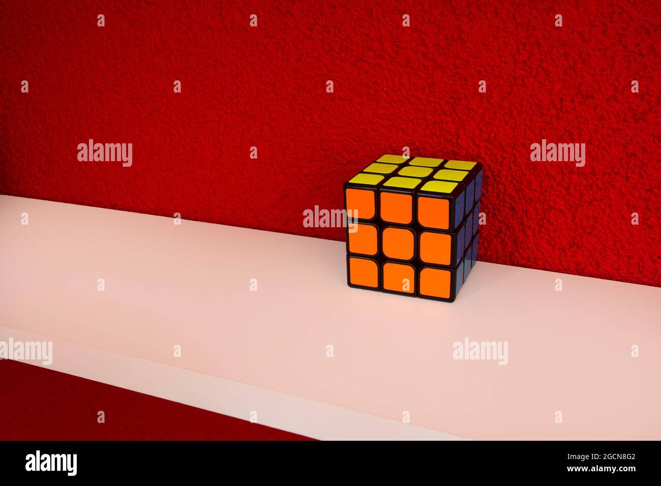 Risolto puzzle velocità cubo su ripiano di legno bianco vicino a parete di colore rosso, colorato rubini cubo con copia spazio mente sfidare Foto Stock
