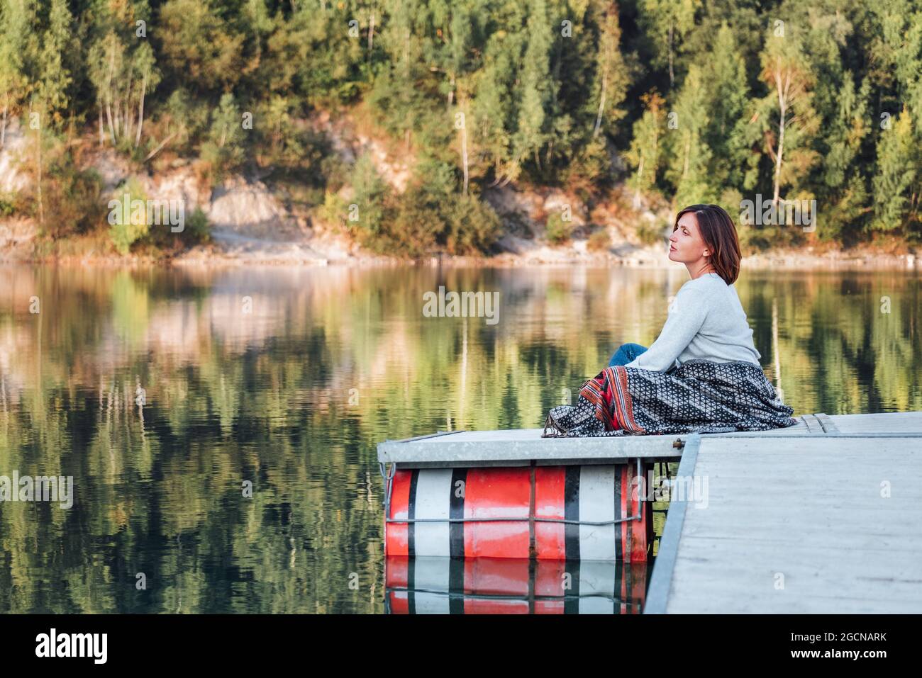 Donna di mezza età sul molo di legno sulla montagna godendo di acque tranquille del lago durante la sua passeggiata nel periodo di stagione autunnale. Tempo libero all'aperto in n Foto Stock