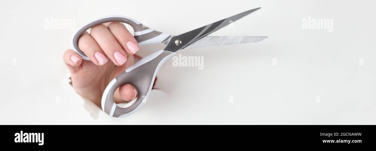 La mano femmina tiene le forbici metalliche in un foro di colore bianco carta Foto Stock