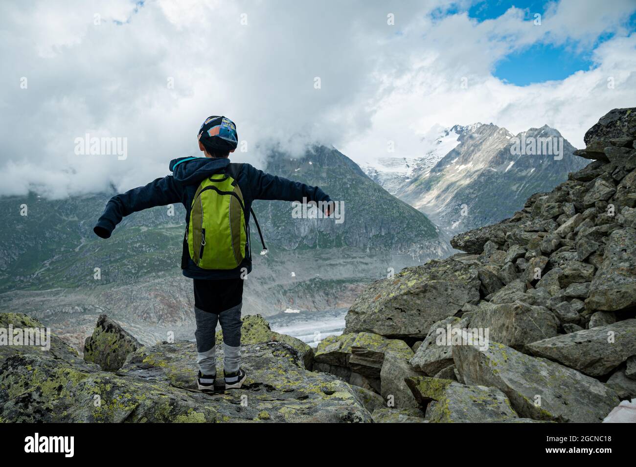 Vista posteriore di un ragazzo con tappo in piedi su rocce e godendo di vista del naturer. Ghiacciaio di Aletsch in Svizzera. Avventura all'aria aperta. Foto Stock