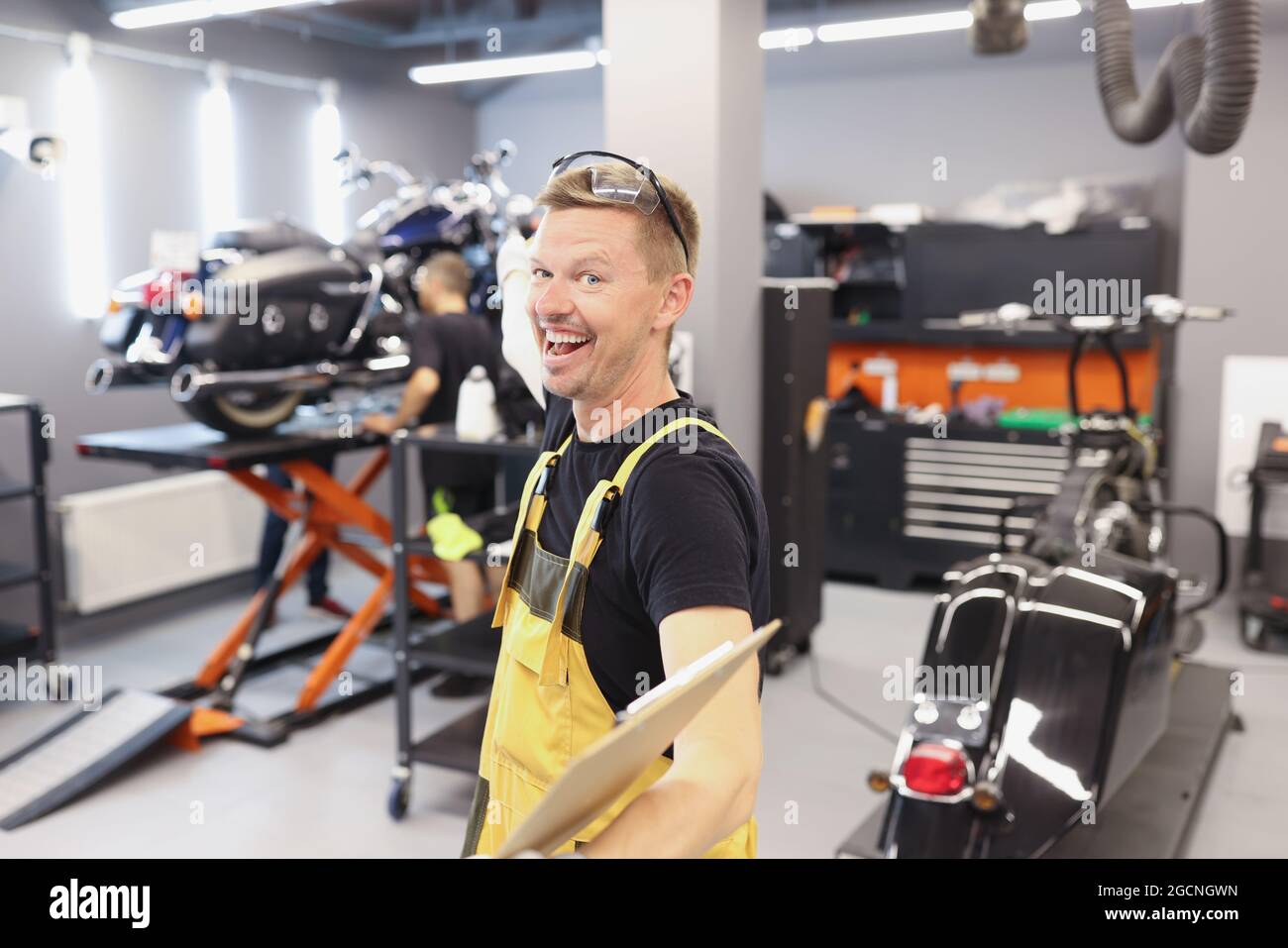 Felice sorridente meccanico automatico o fabbro con appunti in officina Foto Stock