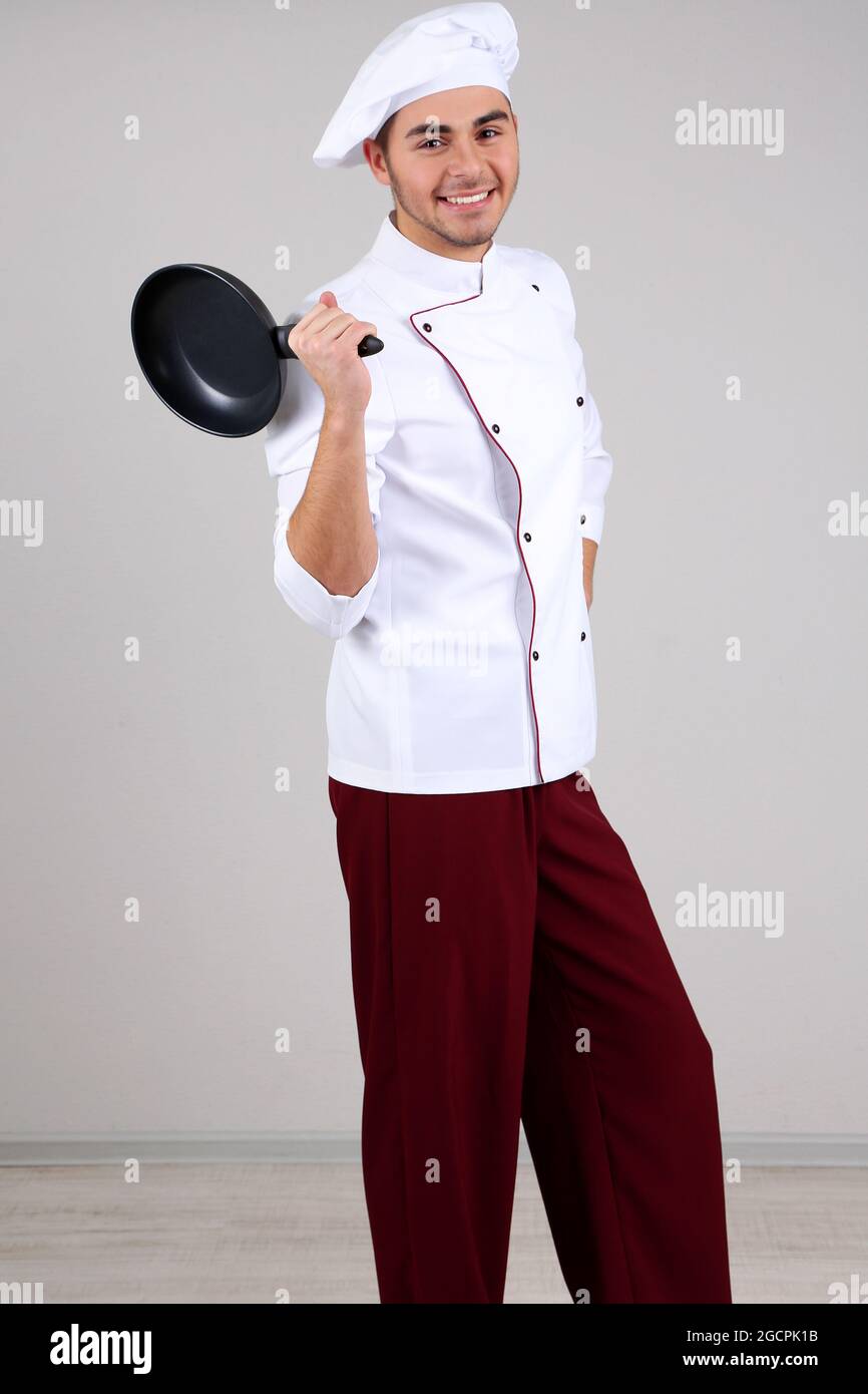 Chef professionista in uniforme bianca e cappello, tenendo la padella in  mano, su sfondo grigio Foto stock - Alamy