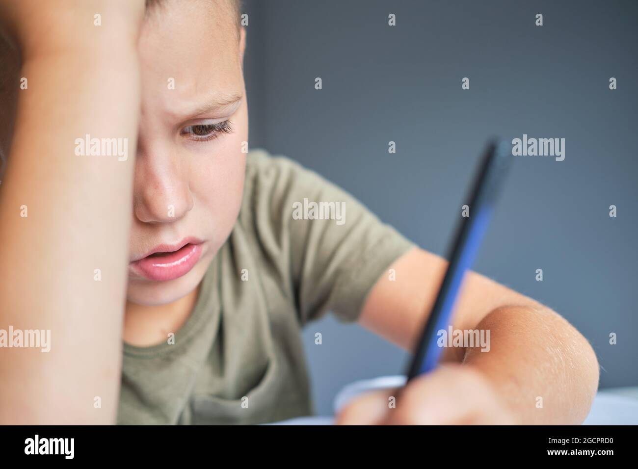 Il ragazzo annoiato e stanco seduto al tavolo e usando il computer portatile mentre fa il lavoro scolastico a casa. Concetto di homeschooling. Foto Stock