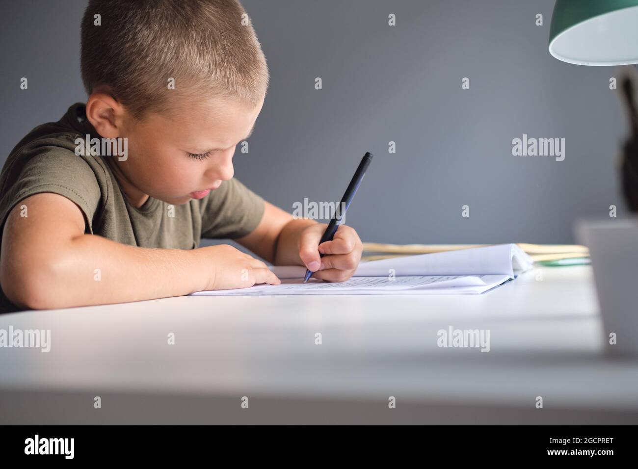 Il ragazzo seduto al tavolo e facendo il lavoro scolastico a casa. Concetto di homeschooling. Foto Stock