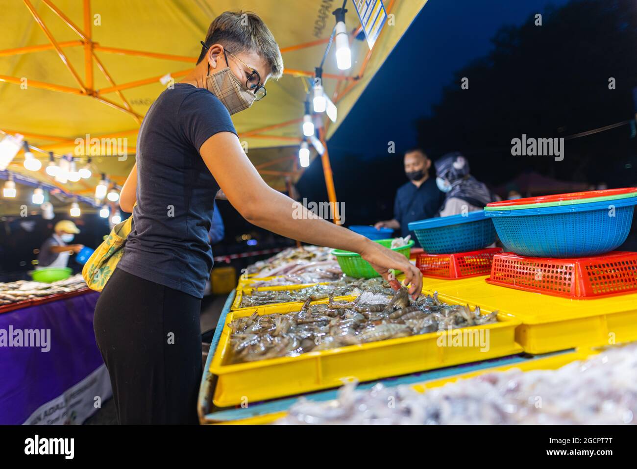 Mercato notturno Street food a Putrajaya, vicino a Kuala Lumpur. Giovane ragazza asiatica acquista frutti di mare in un mercato notturno. Donne malesi con maschera facciale in una strada Foto Stock