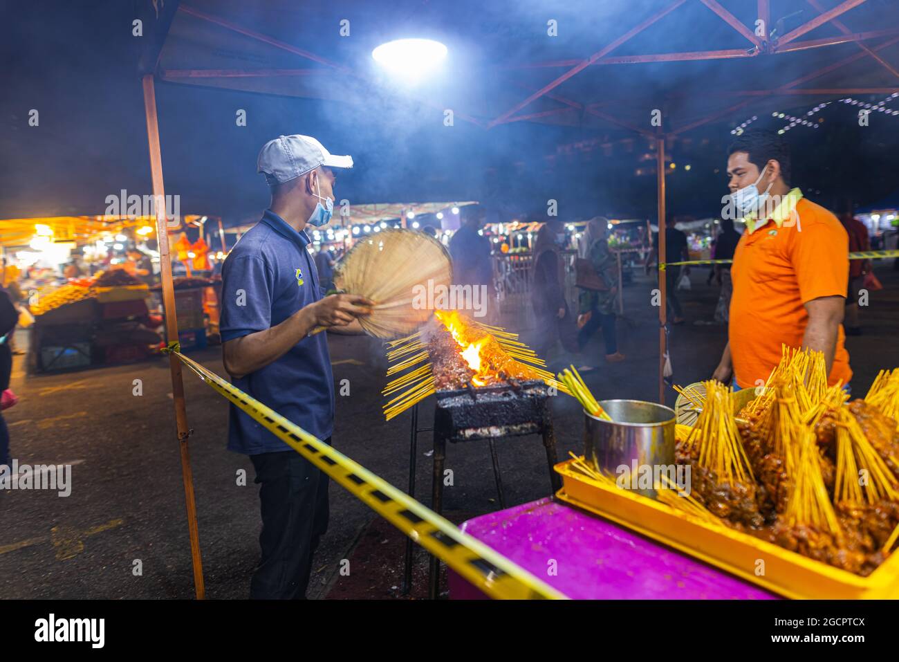 Mercato notturno Street food a Putrajaya, vicino a Kuala Lumpur. Due giovani uomini che fanno spiedini satay su una griglia a fuoco aperto. Il satay è un piatto tradizionale malese Foto Stock