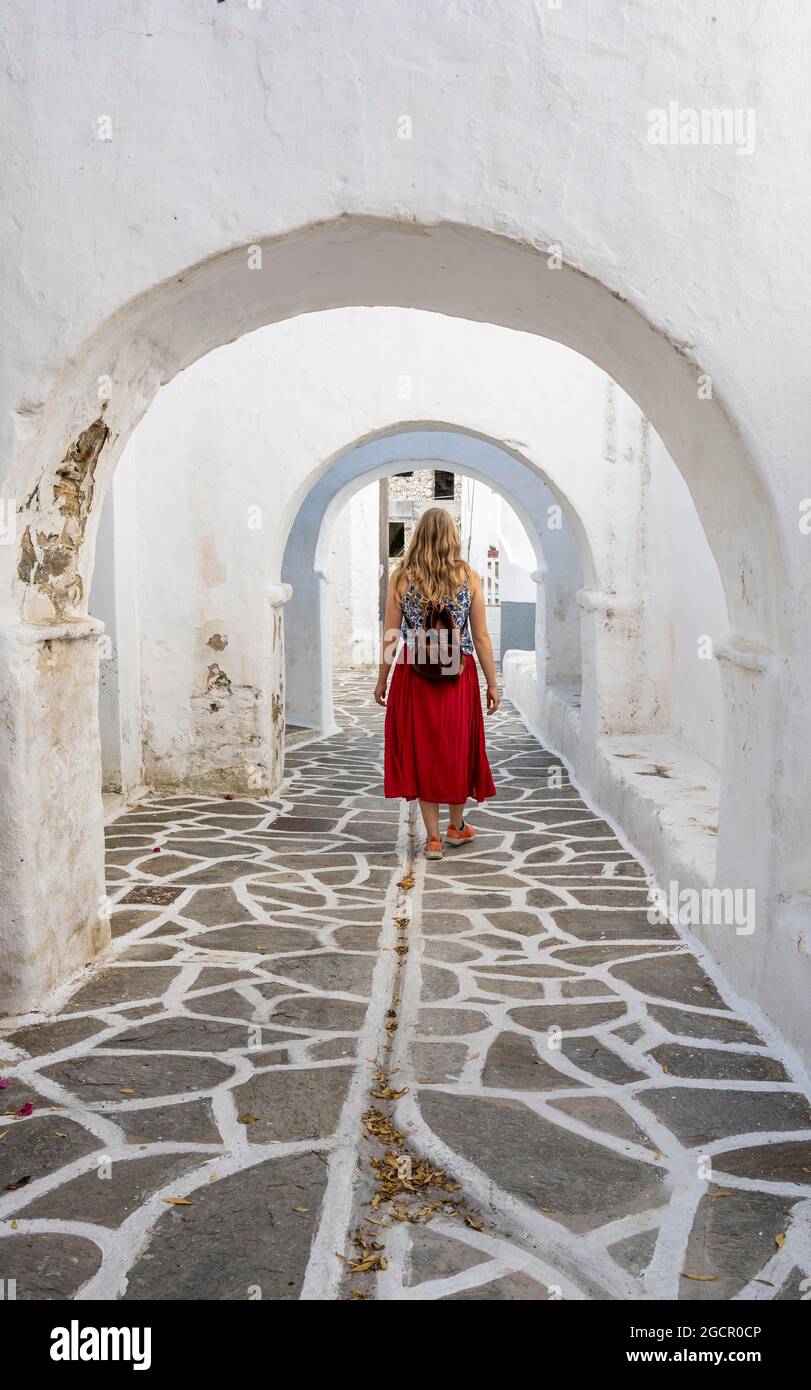 Archi bianchi tra case, giovane donna con abito rosso nel centro storico di Lefkes, Paros, Cicladi, Grecia Foto Stock