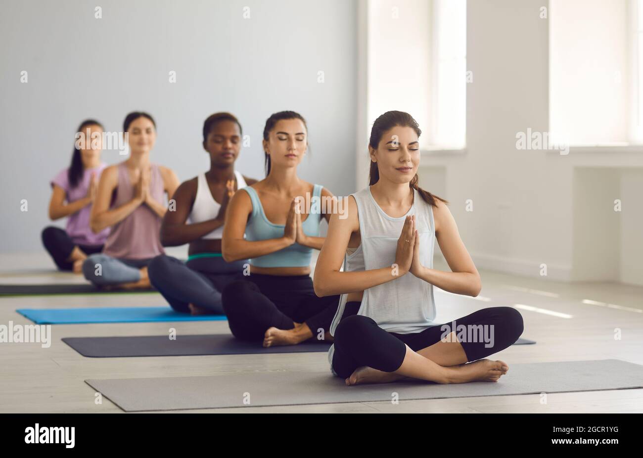 Le giovani donne multirazziali atletiche praticano lo yoga insieme in un moderno studio di luce. Foto Stock