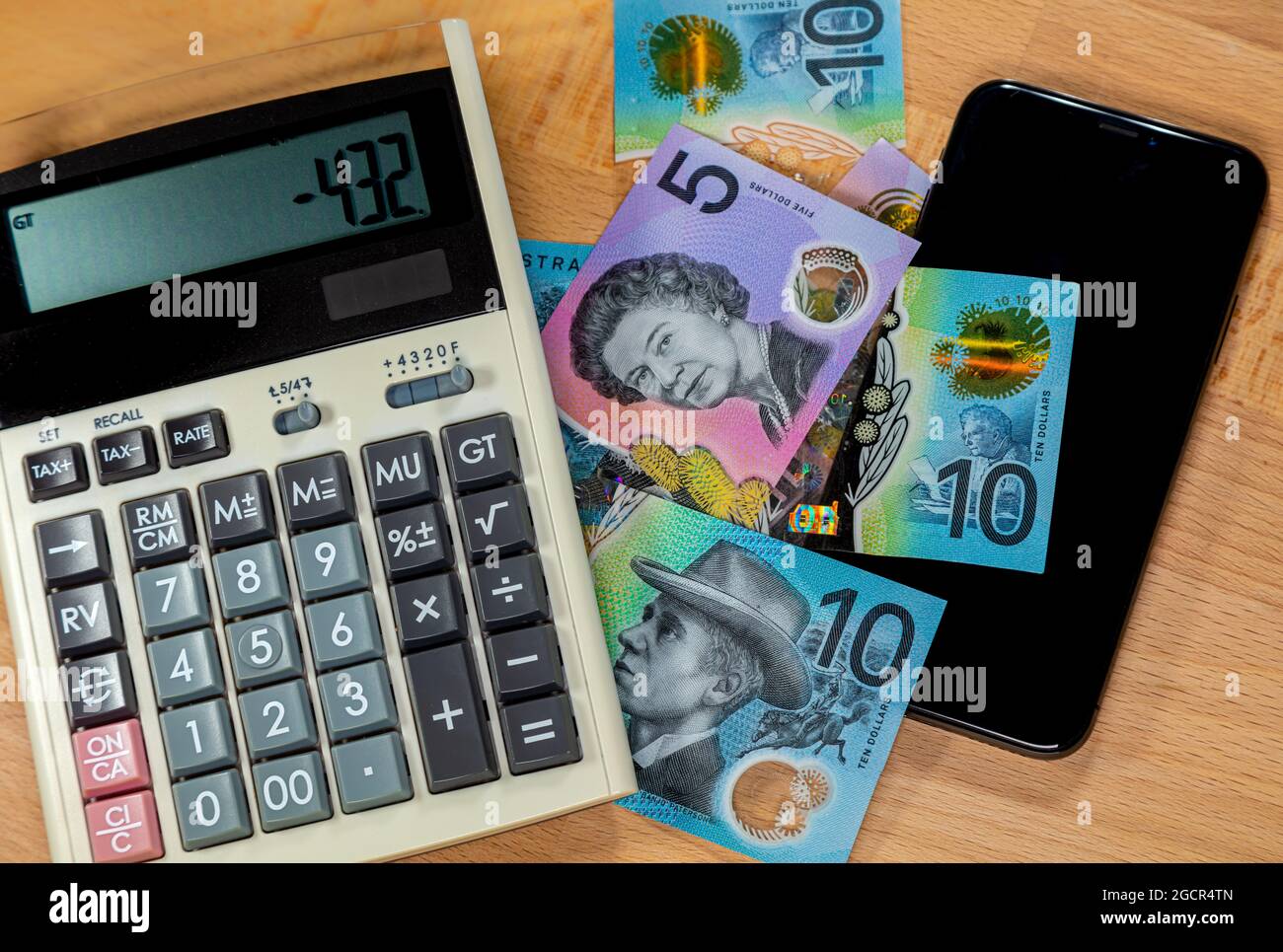 Dollaro australiano su una scrivania in legno, circondato da calcolatrice e un telefono cellulare. Primo piano macrofotografia di banconote e utilli da ufficio su una t di legno Foto Stock