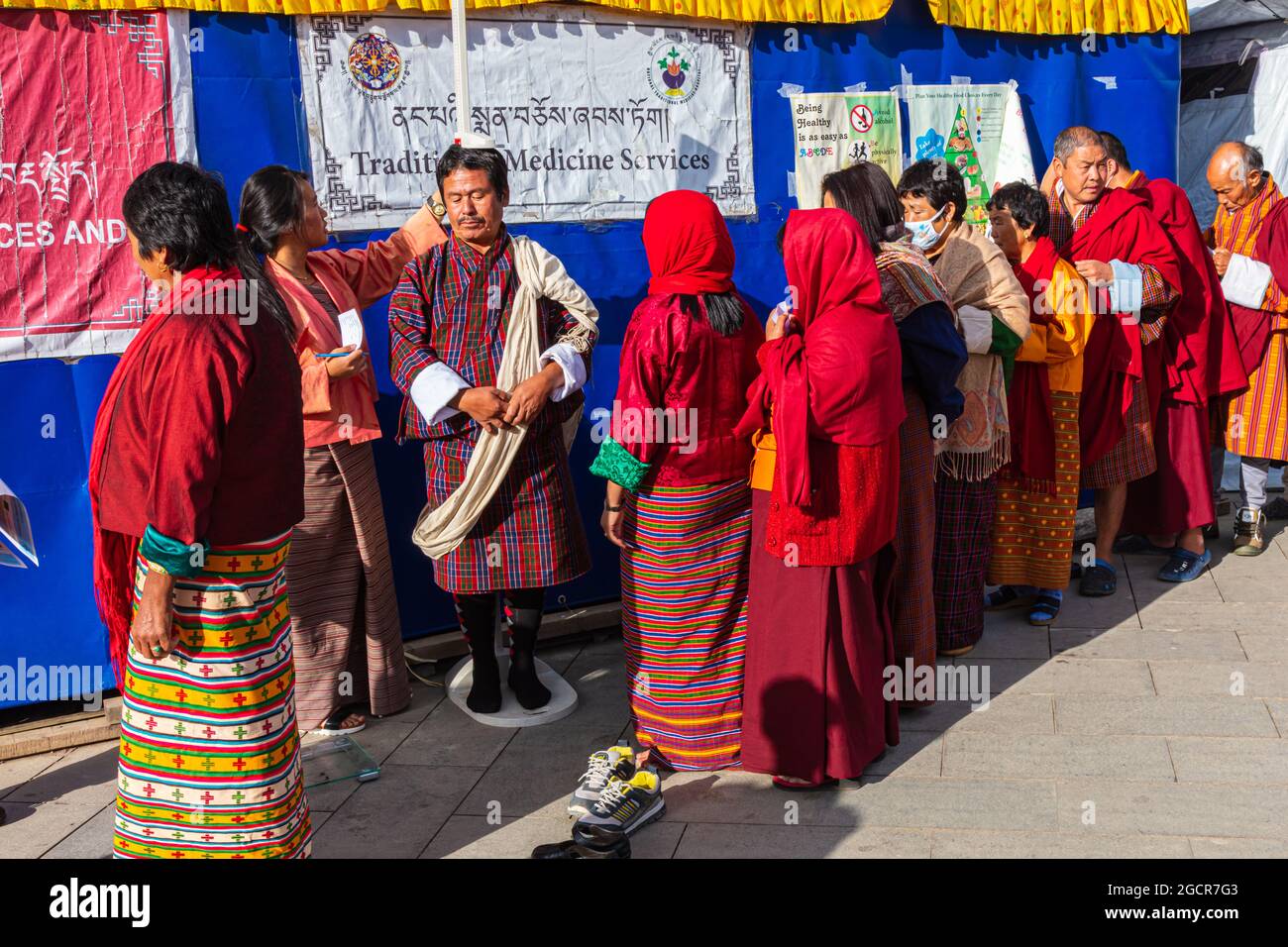 Paro, Bhutan - 12 febbraio 2021 - controllo di salute prima di una cerimonia di preghiera buddista. Le persone in Bhutanese tradizionale rosso accappatoio in fila per medic Foto Stock
