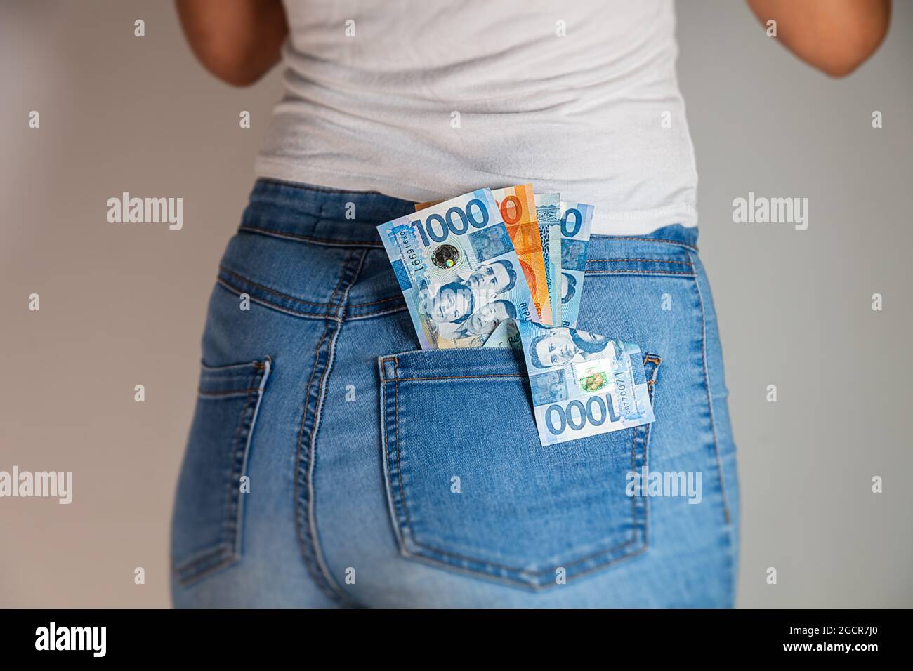 Filippine peso in una tasca di jeans femminile. Le note di pesos filippini sono bloccate in una tasca di jeans donna. Pesos in una tasca di natiche dei pantaloni in denim di una ragazza. Soldi i Foto Stock