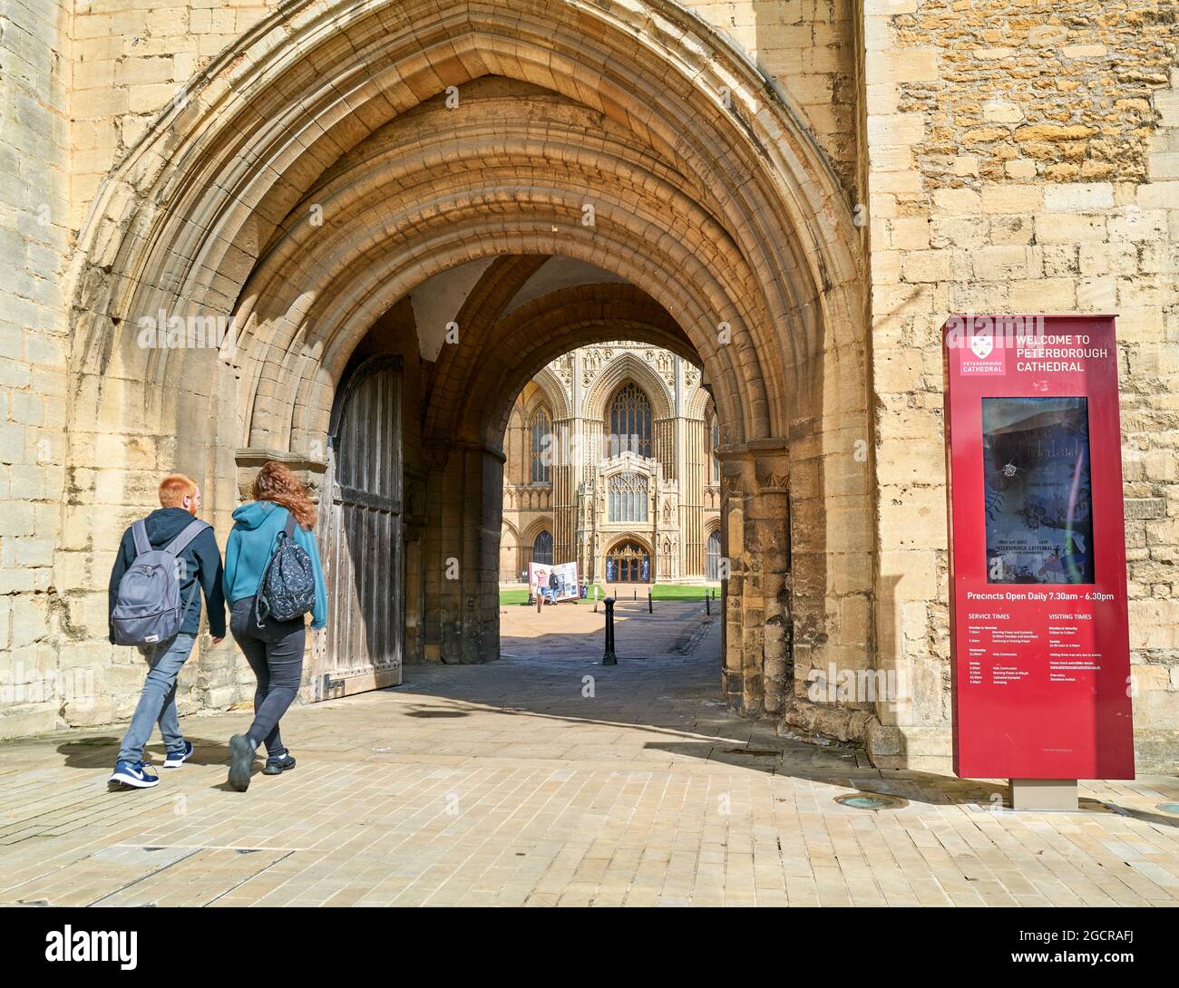Un paio di visitatori passa attraverso l'ingresso ad arco dei quartieri e della cattedrale di San Pietro, San Paolo e Sant'Andrea a Peterborough, Inghilterra. Foto Stock