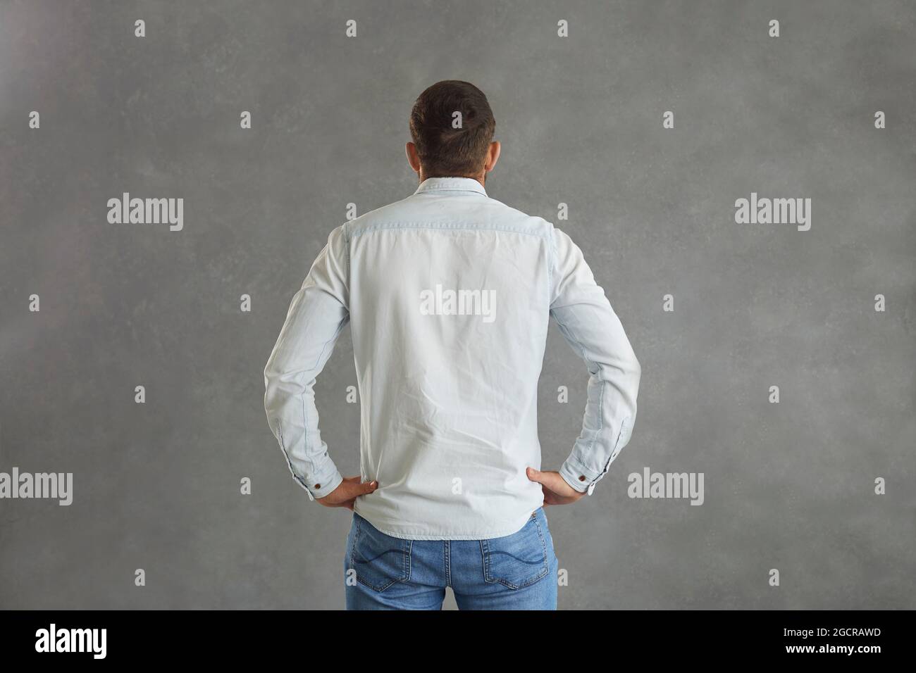 Vista posteriore di uomo in camicia in denim in piedi mani su fianchi isolati su sfondo grigio Foto Stock