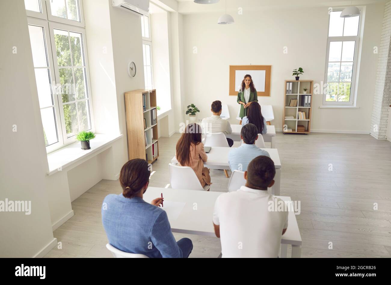 Gruppo di studenti adulti che hanno una lezione seduto alle scrivanie in un moderno interno dell'aula Foto Stock