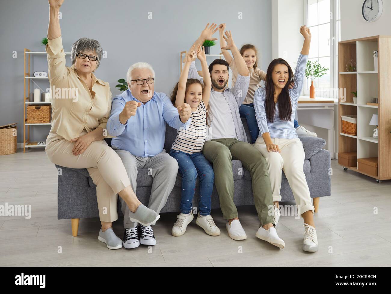 Grande famiglia di generazioni diverse che guardano emotivamente una partita sportiva in TV a casa. Foto Stock