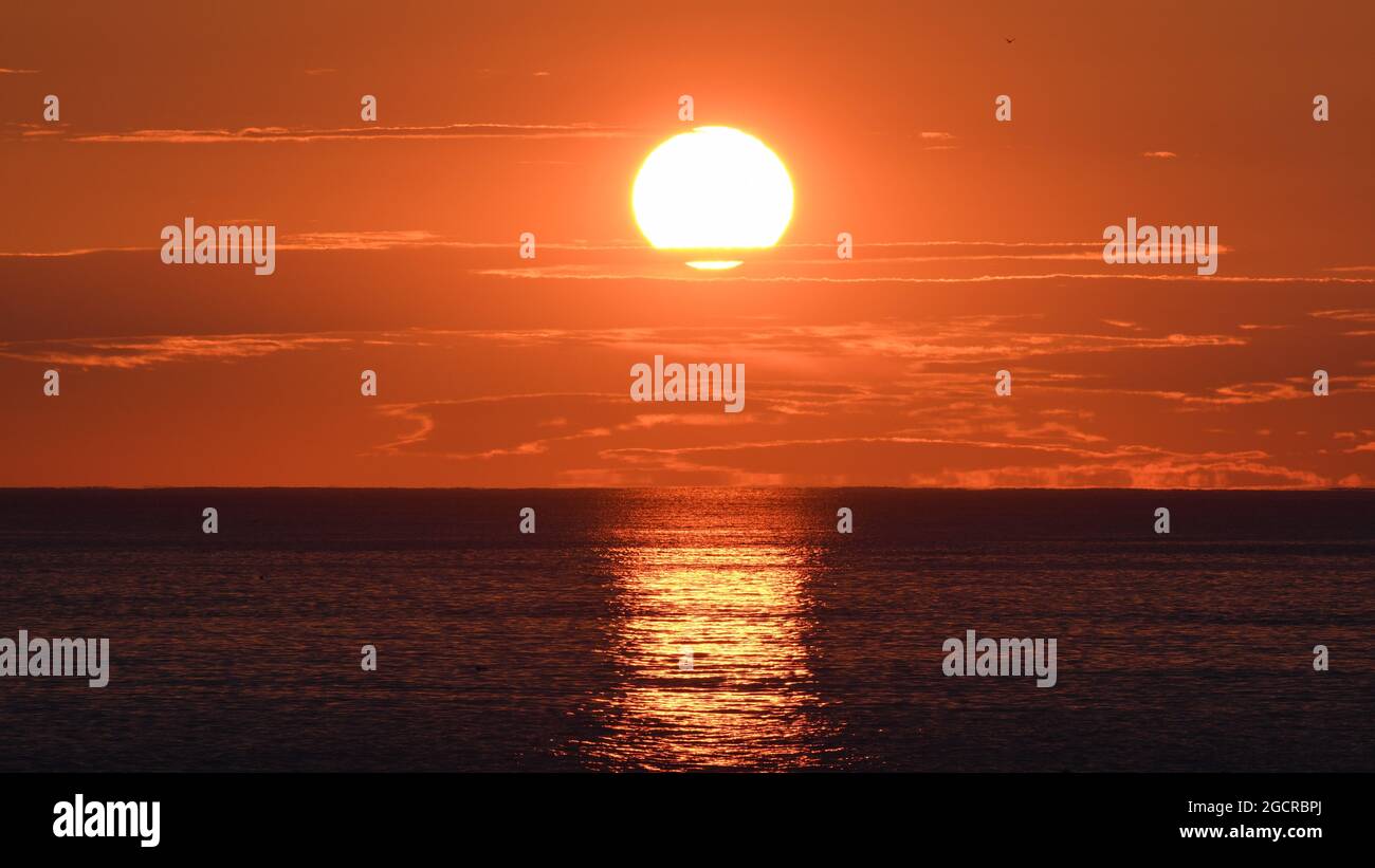 Il grande sole arancione illumina l'alba sull'Atlantico Foto Stock
