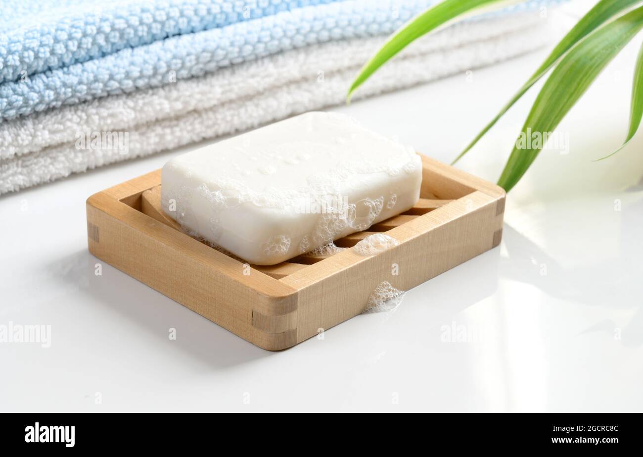 Saponetta bianca con schiuma su una tovaglietta di sapone in legno e  tovaglioli di cotone su un tavolo bianco Foto stock - Alamy