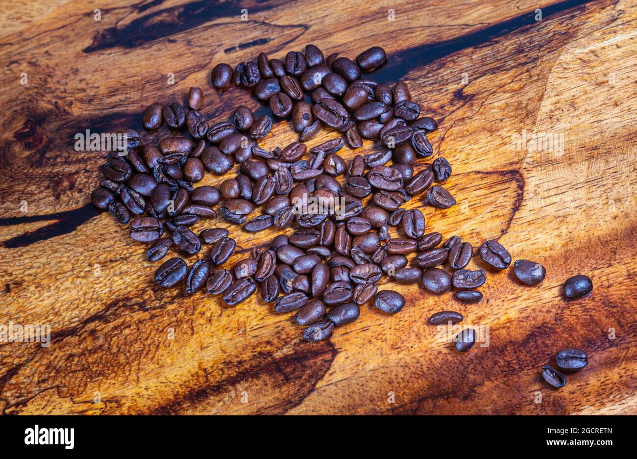 Macro fotografia vista dall'alto di un mucchio di chicchi di caffè appena tostati su sfondo di legno. Primo piano dettagliato ad alta risoluzione di chicchi di caffè tostati marroni Foto Stock