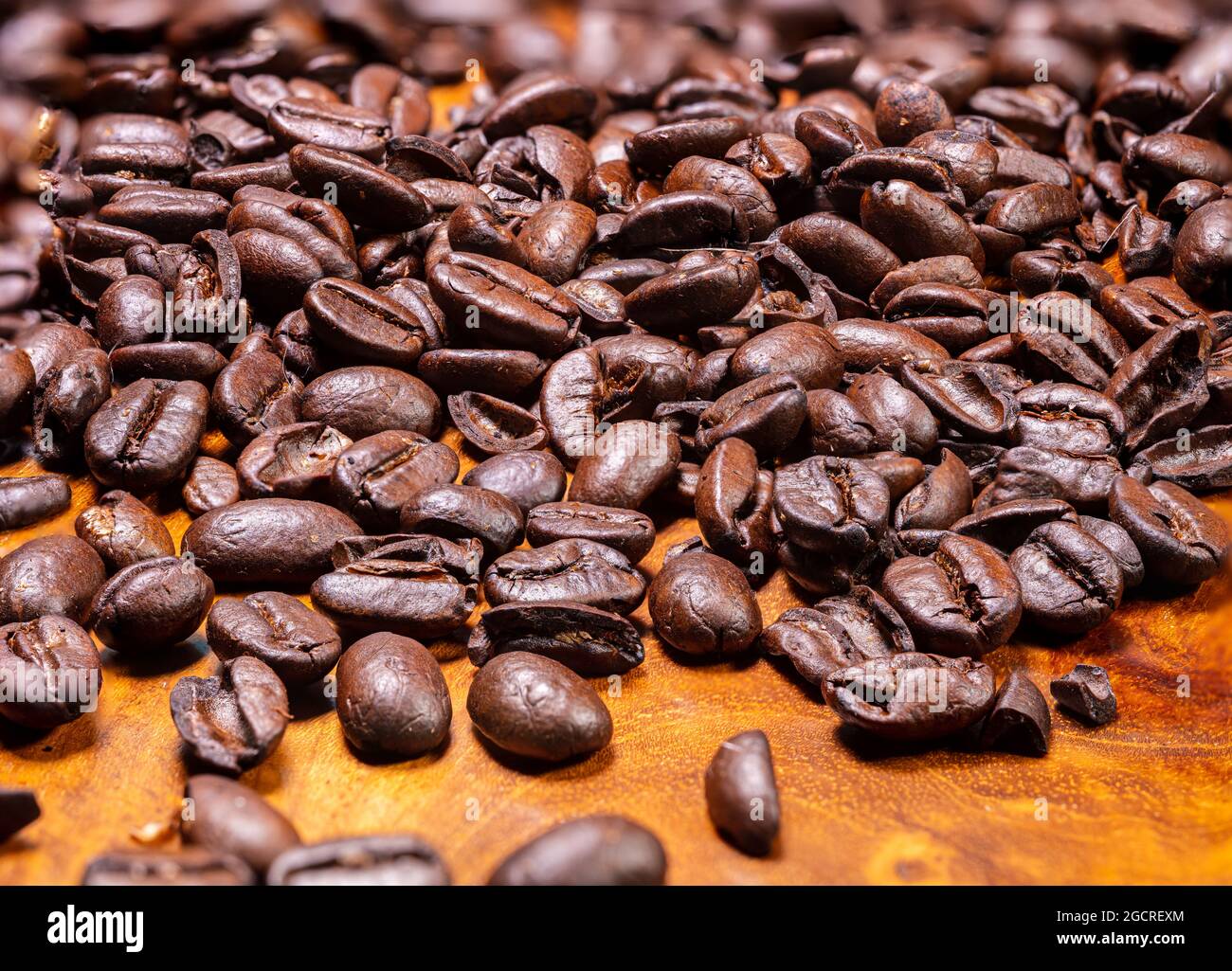 Macro fotografia di un mucchio di chicchi di caffè appena tostati su sfondo di legno. Primo piano dettagliato ad alta risoluzione dei chicchi di caffè tostati marroni sulla trop Foto Stock