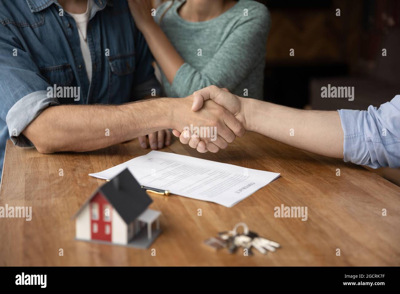 Coppia di clienti e broker immobiliare che dà handshakes Foto Stock