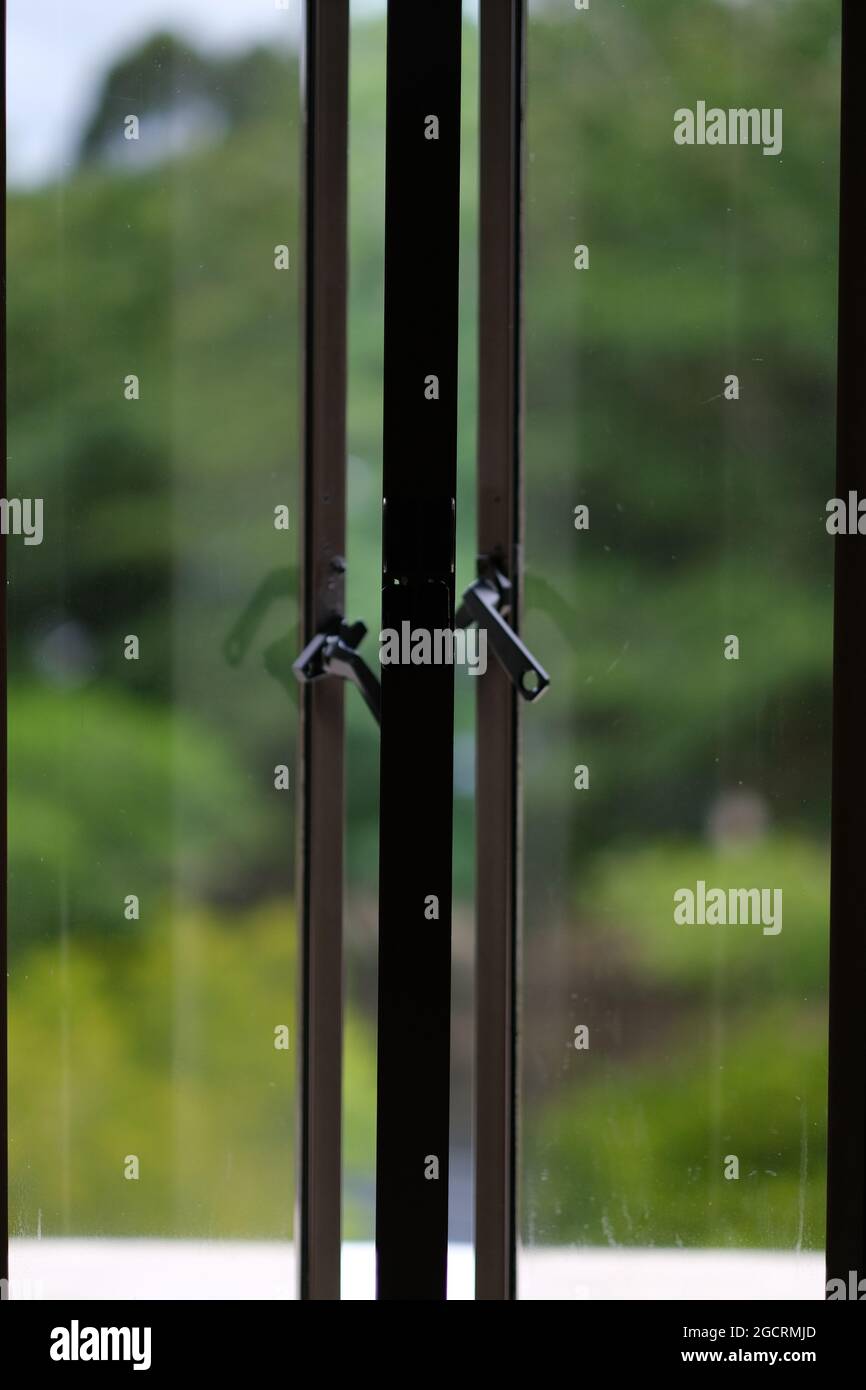 Una finestra leggermente aperta a due ali, con giardino sfocato dietro di essa Foto Stock