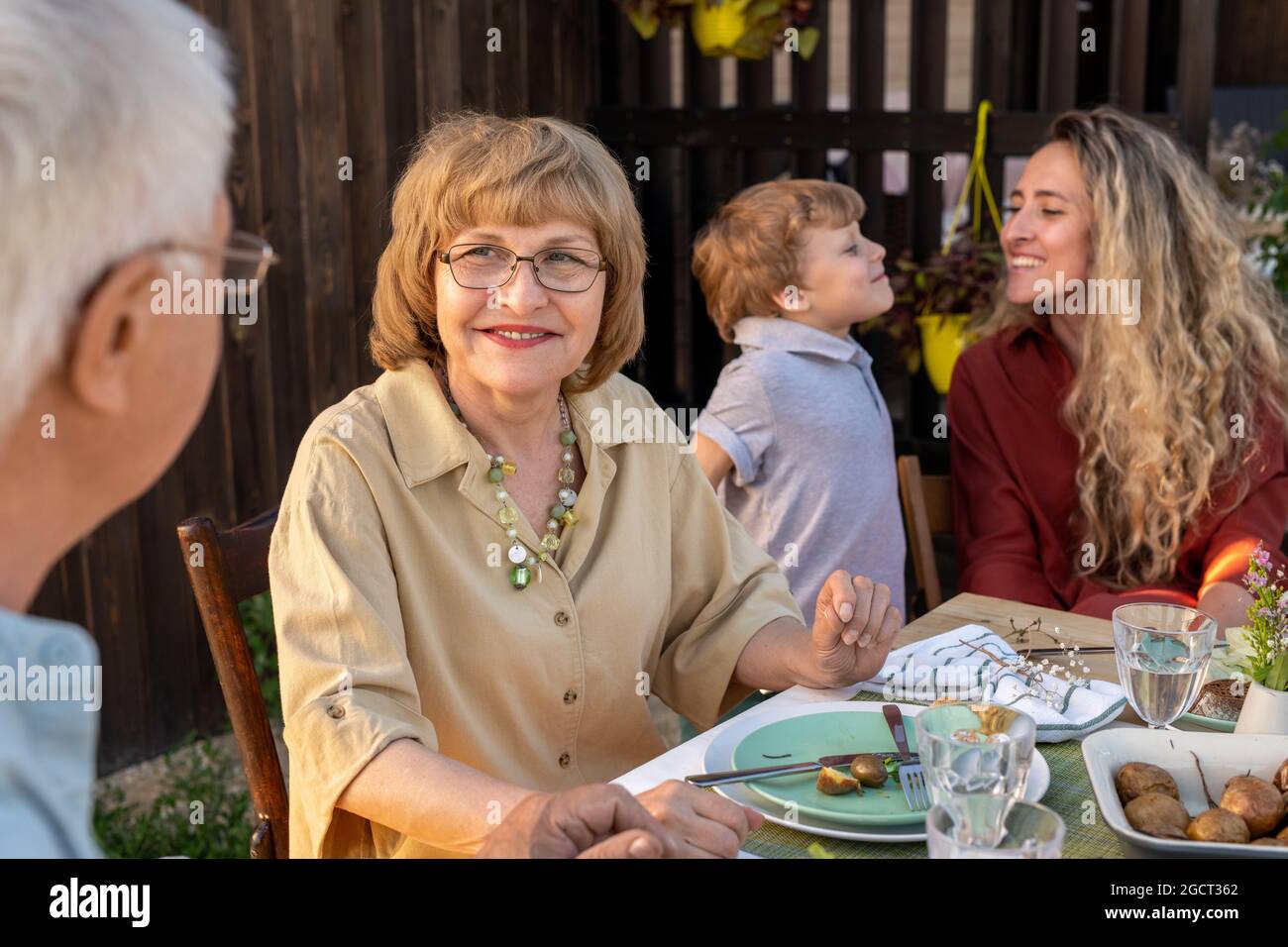 Felice donna matura che parla con suo marito da tavolo servito durante la cena all'aperto Foto Stock