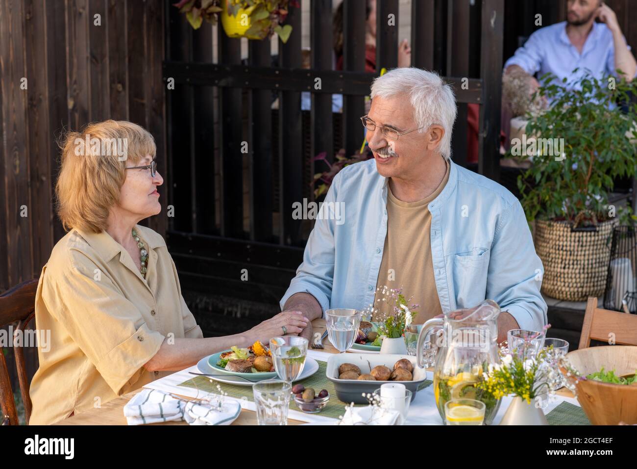 Gli anziani felici discutono la loro vita di famiglia dopo cena dalla loro casa di campagna durante il fine settimana Foto Stock