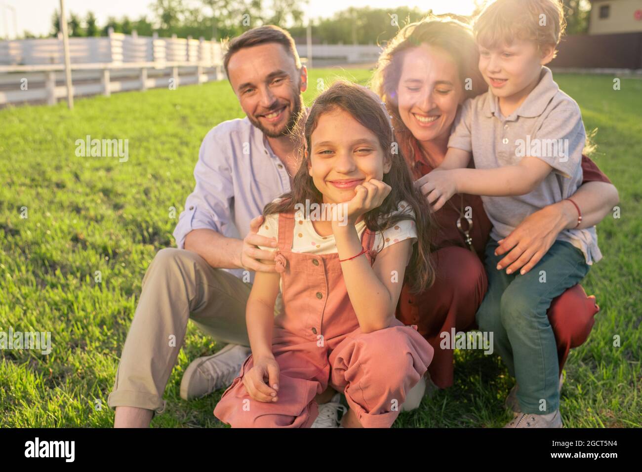 Carina bambina, suo fratello e i genitori seduti sul prato verde di fronte alla macchina fotografica Foto Stock