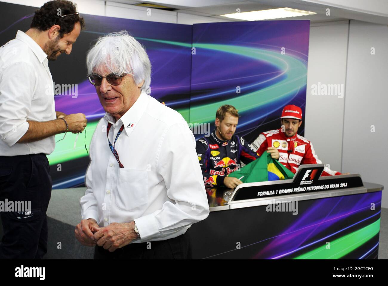 Bernie Ecclestone (GBR) il CEO di Formula One Group (FOM) presenta una bandiera brasiliana, firmata da sé e da tutti i piloti, per Sebastian Vettel (GER) Red Bull Racing a firmare, da presentare a Mark Webber (AUS) Red Bull Racing. Gran Premio del Brasile, domenica 24 novembre 2013. San Paolo, Brasile. Foto Stock