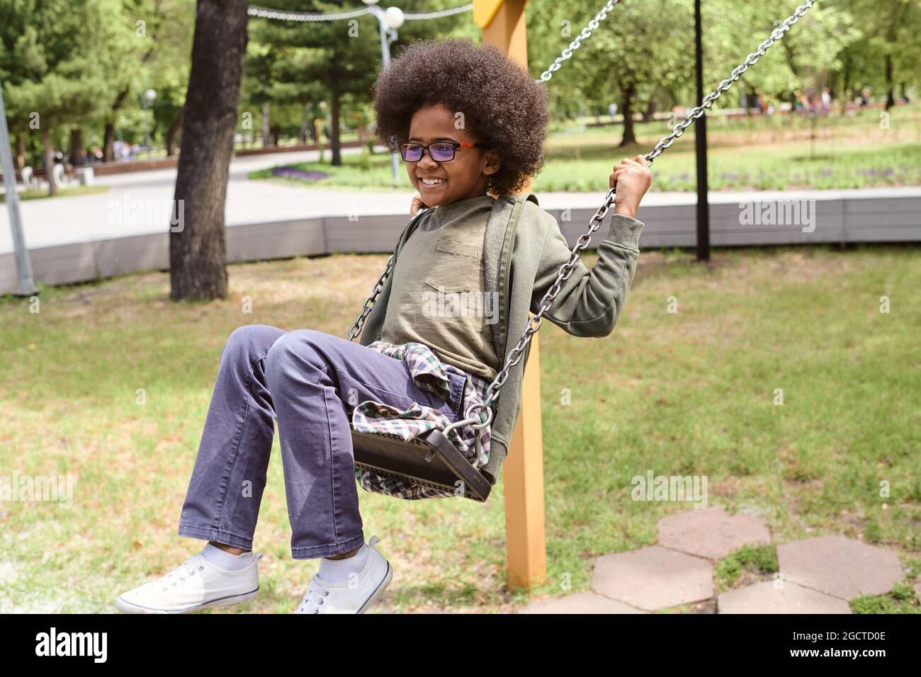 Adorabile ragazzino che oscilla nel parco tra prati verdi il giorno d'estate Foto Stock