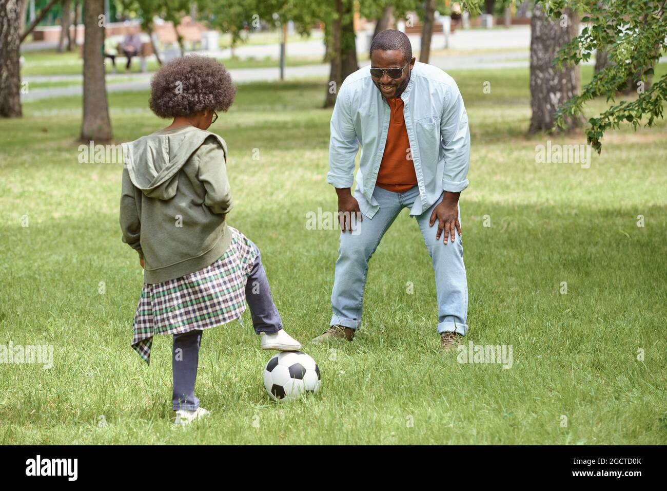 Il ragazzino e suo padre giocano a calcio su un prato verde in ambiente urbano Foto Stock