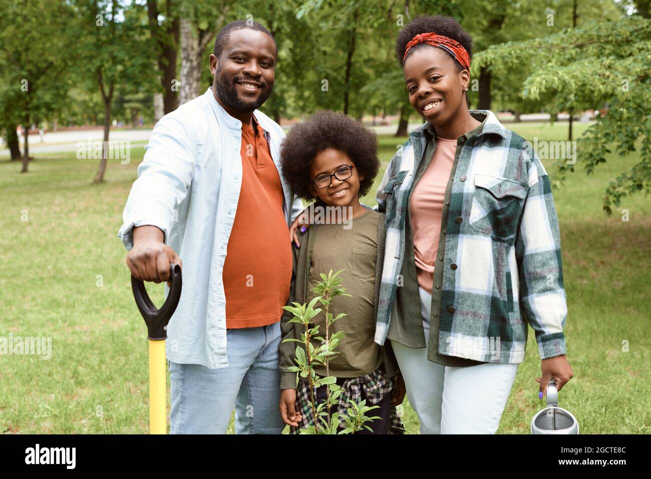 Giovane allegra famiglia di etnia africana che va a piantare un piccolo albero nel parco Foto Stock