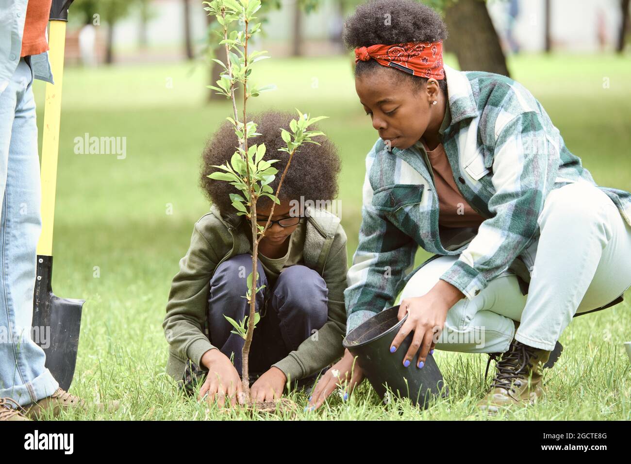 Giovane femmina e suo figlio piccolo che piantano l'albero in uno dei parchi della città il giorno d'estate Foto Stock
