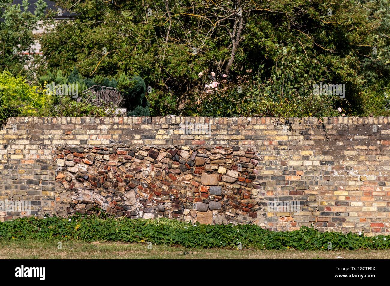Una sezione di parete fatta da un jumble di pietre nel mezzo di un muro normale di mattone. Cambridge, Regno Unito Foto Stock