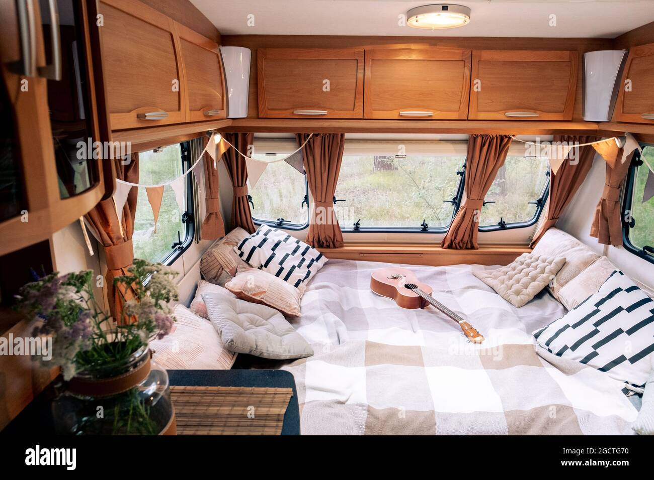 Interno di casa di viaggio con cuscini e chitarra su grande letto e mobili in legno intorno Foto Stock