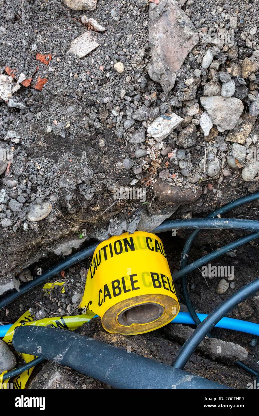 In un foro scavato durante i lavori di costruzione su una proprietà domestica cavi, tubi e un rotolo di nastro di attenzione giallo può essere visto. Cambridge, Regno Unito Foto Stock