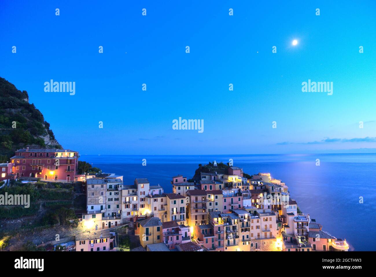 Luna sul mare e il piccolo borgo di Manarola, il Parco Nazionale delle cinque Terre, la Liguria, l'Italia come la luce del giorno si affievolisce Foto Stock