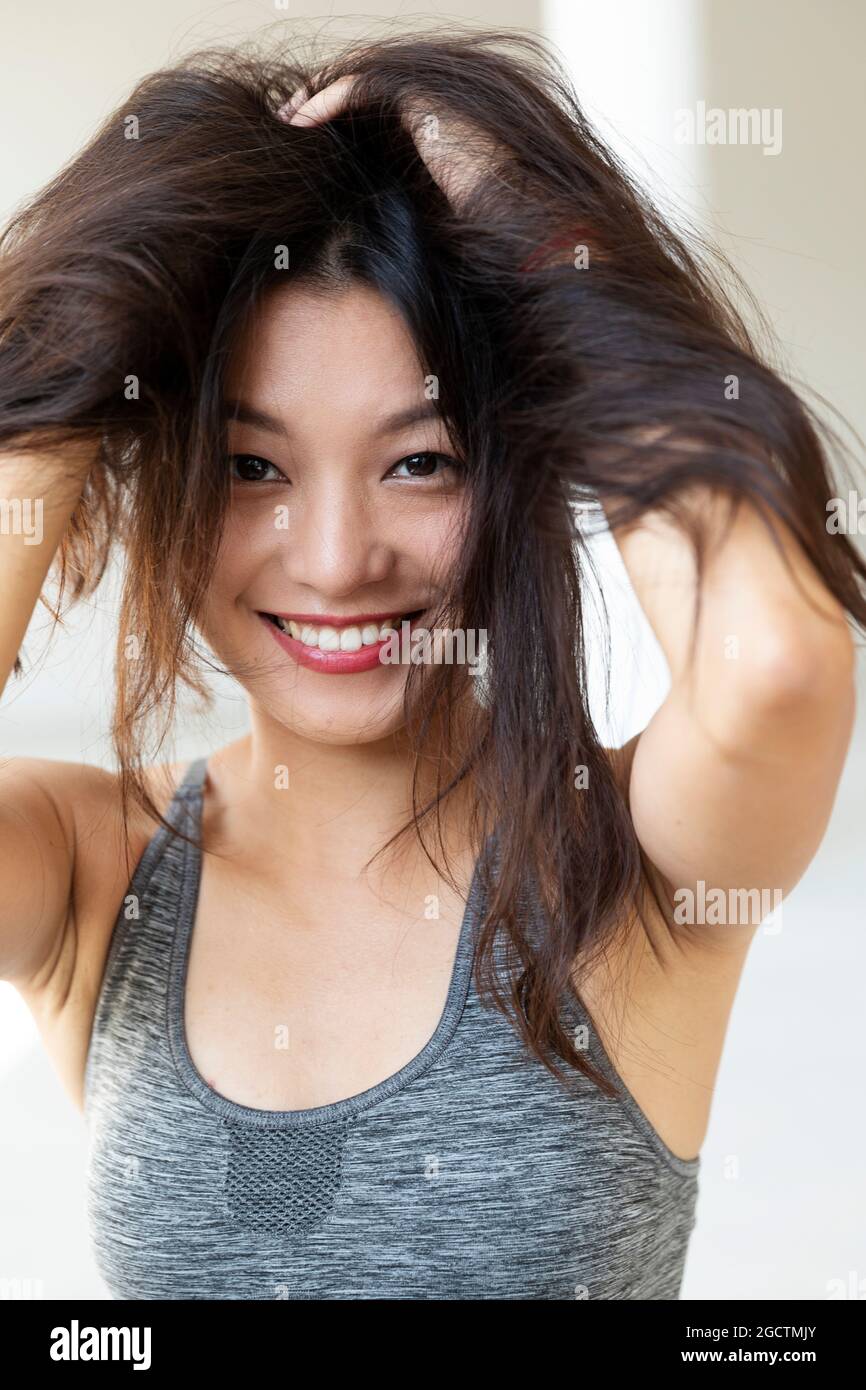 Giovane bella ragazza asiatica sorride e gioca con i suoi capelli. Indossa una parte superiore sportiva e un rossetto rosso. Isolato Foto Stock