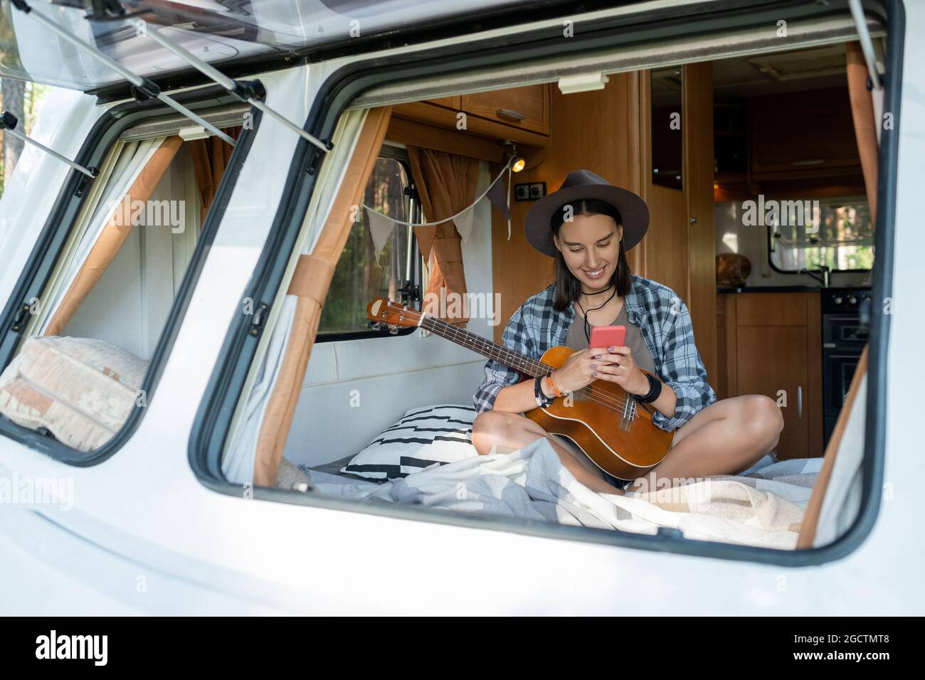 Felice giovane femmina con la chitarra a scorrimento in smartphone all'interno della casa su ruote Foto Stock