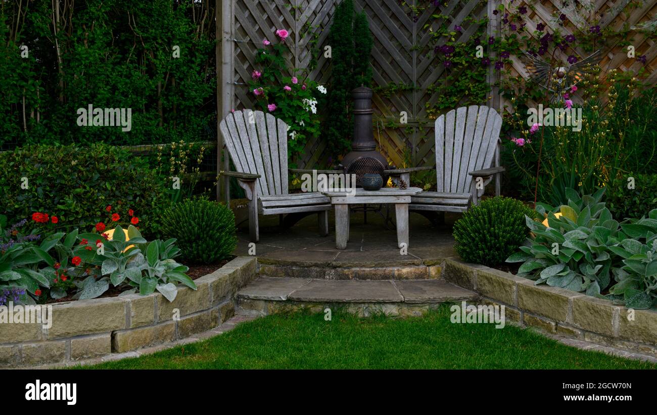 Bellissimo giardino paesaggistico colorato (design contemporaneo, pareti curve, chiminea ornamentale, terrazze, luci illuminate al tramonto) - Yorkshire Inghilterra UK Foto Stock
