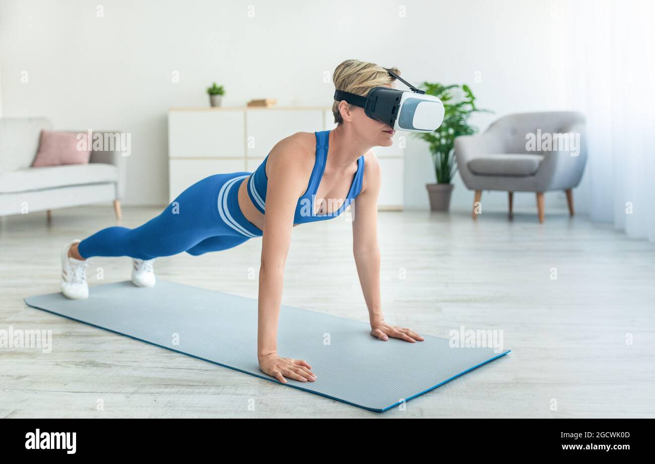 Donna focalizzata nel visore VR che si esercita a casa Foto Stock