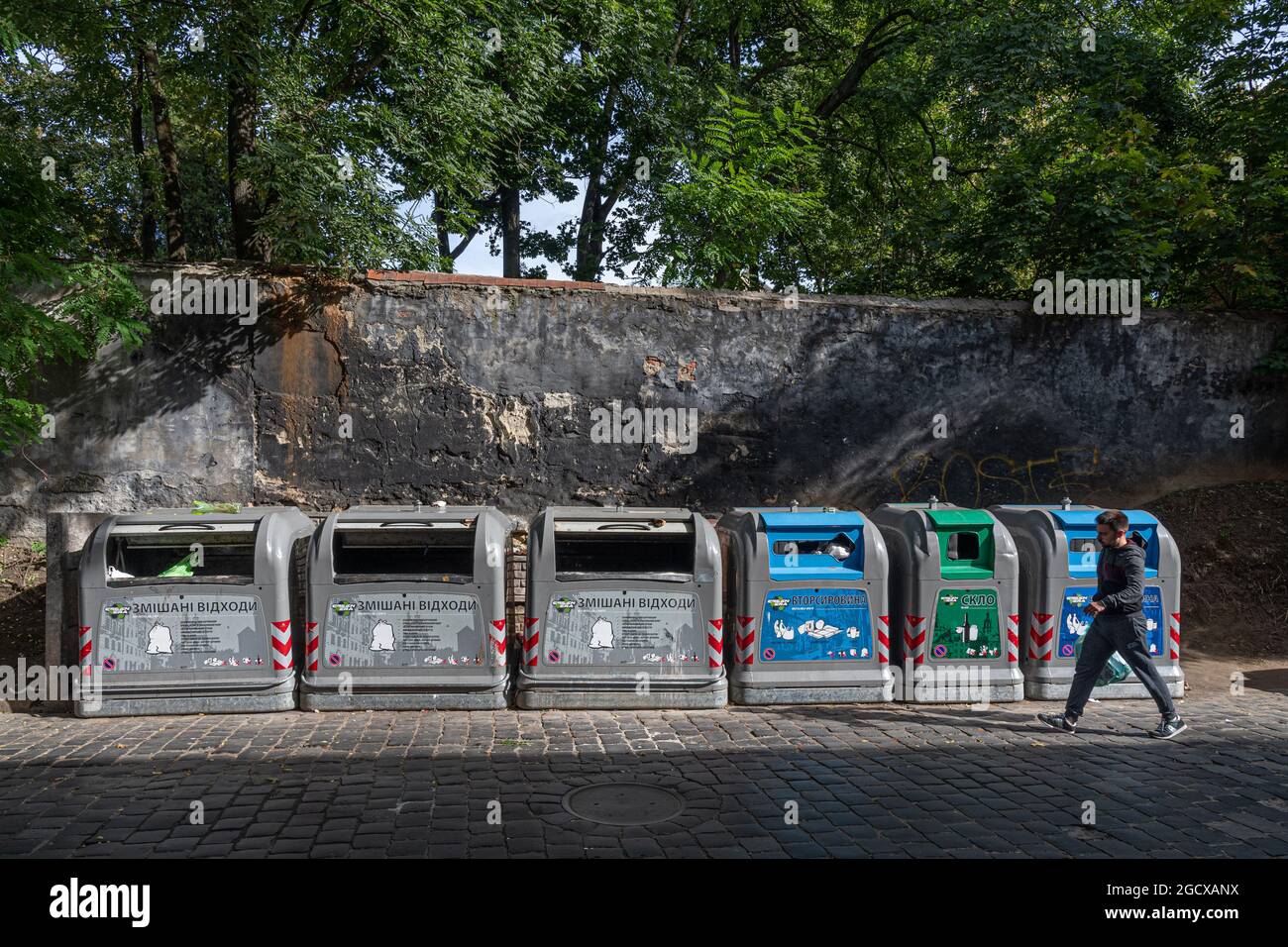 Fila di bidoni di rifiuti diversi per rifiuti ordinati a riciclaggio. L'uomo va con il sacchetto della lettiera per gettarlo nella lattina della spazzatura per il riciclaggio separato. Ambientale Foto Stock