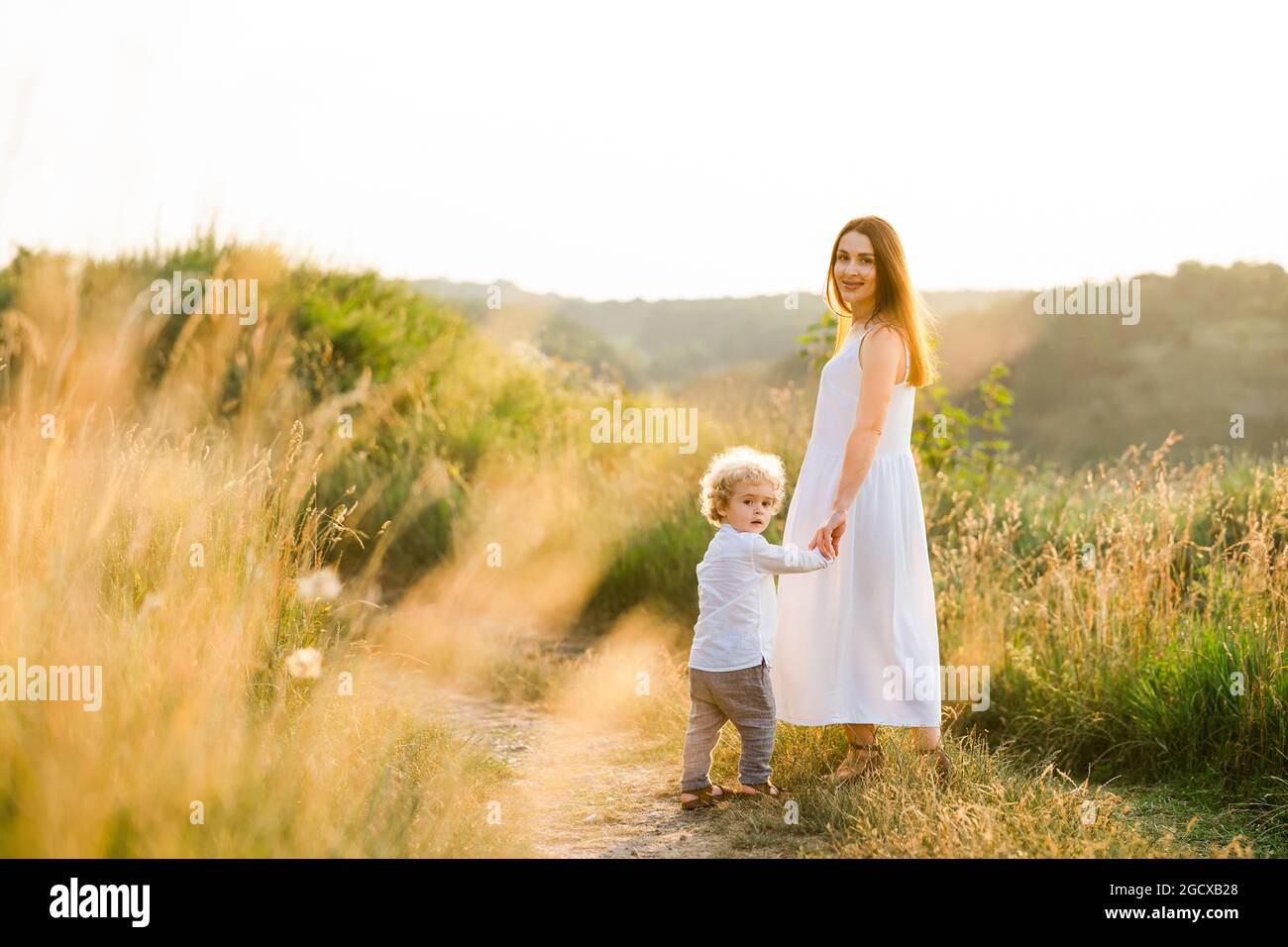 Madre felice e figlio stanno camminando nel campo pittoresco al tramonto Foto Stock