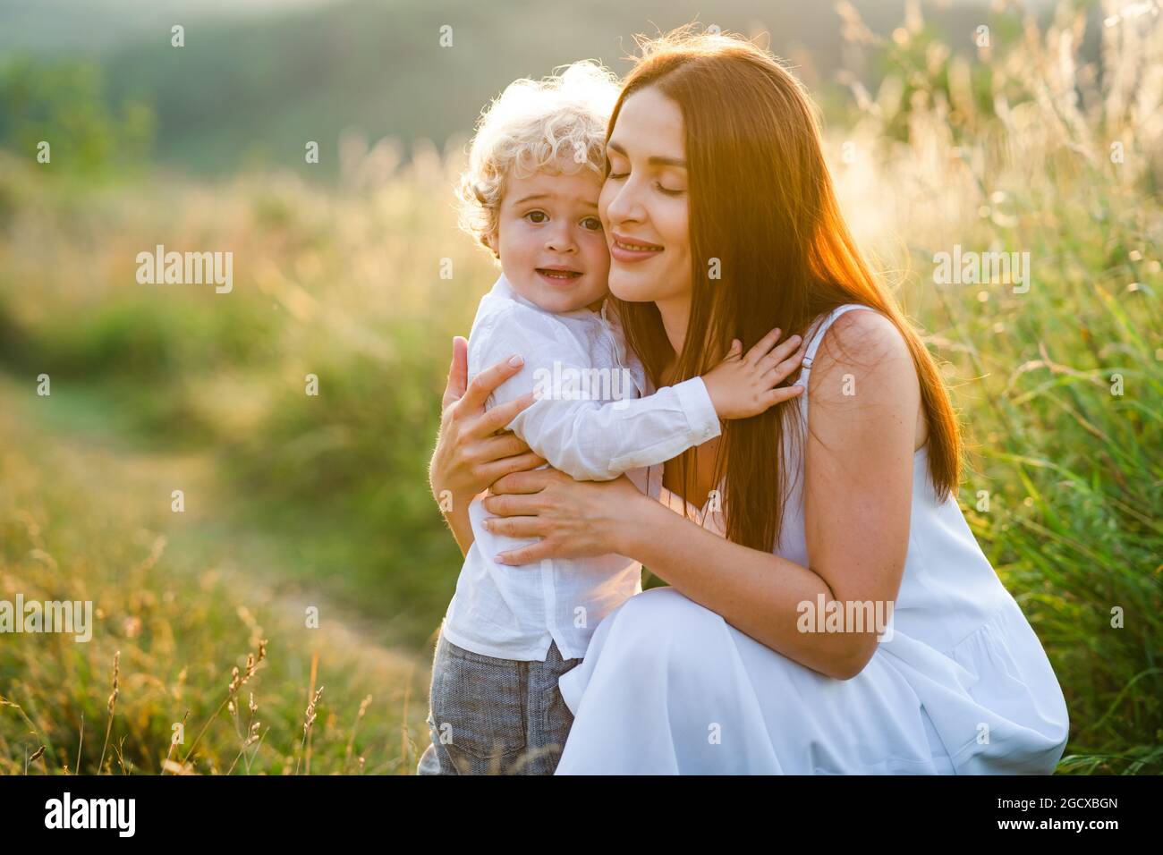 La madre amorevole abbraccia suo figlio mentre cammina in un campo pittoresco Foto Stock