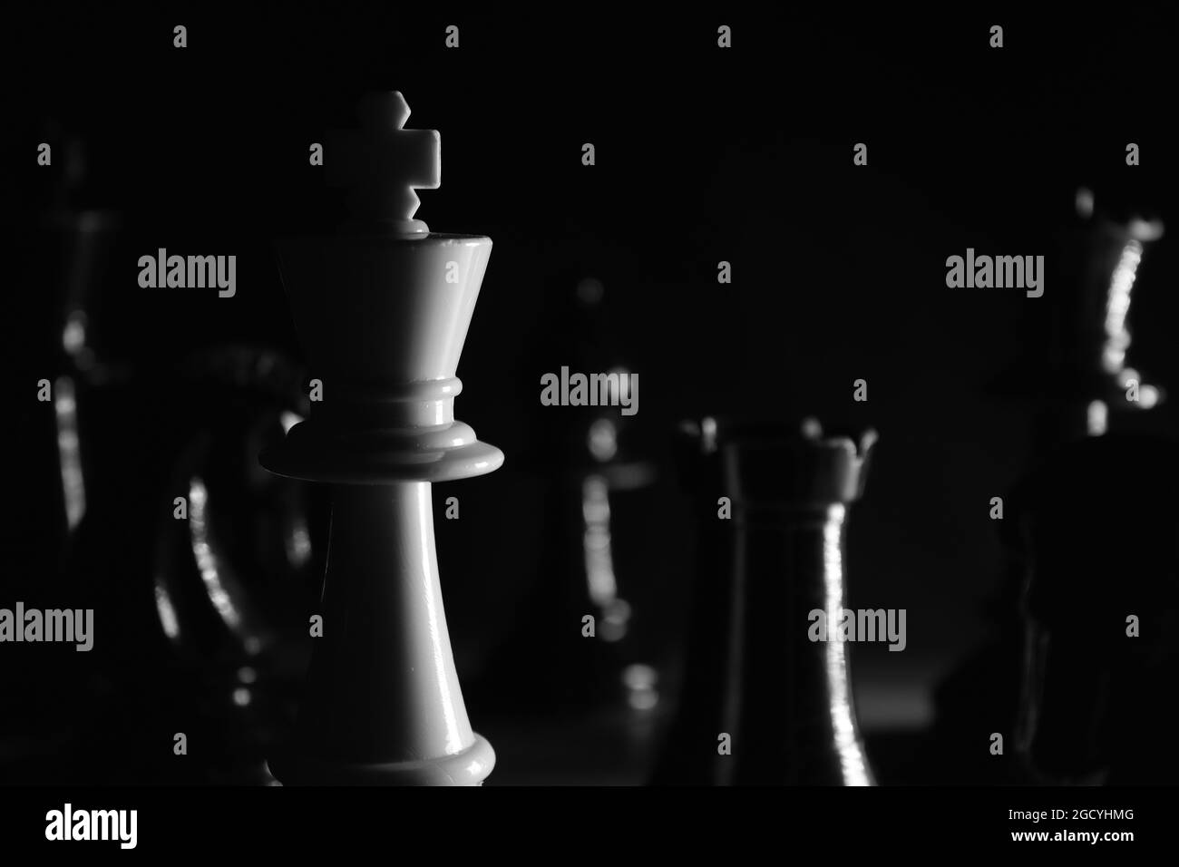 Scacchi bianchi pezzo della regina in bianco e nero primo piano circondato da pezzi neri, gettato in ombra Foto Stock