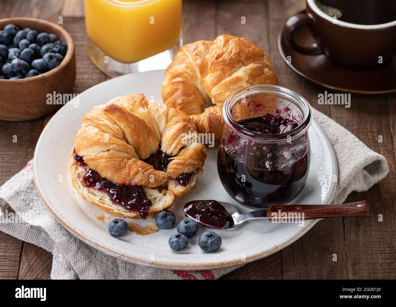 Croissant, mirtilli e marmellata di mirtilli su un piatto con succo d'arancia e caffè sullo sfondo Foto Stock
