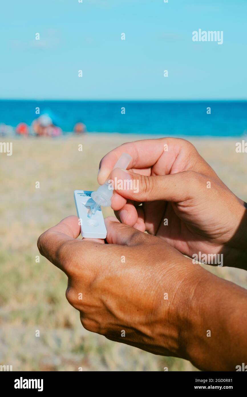 primo piano di un giovane caucasico sulla spiaggia mettendo il proprio campione nel dispositivo di test diagnostico dell'antigene covid-19 Foto Stock