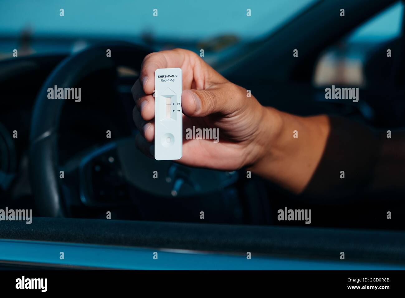 un giovane caucasico, seduto al posto di guida della sua auto, mostra un covid-19 dispositivo di prova con un risultato negativo Foto Stock