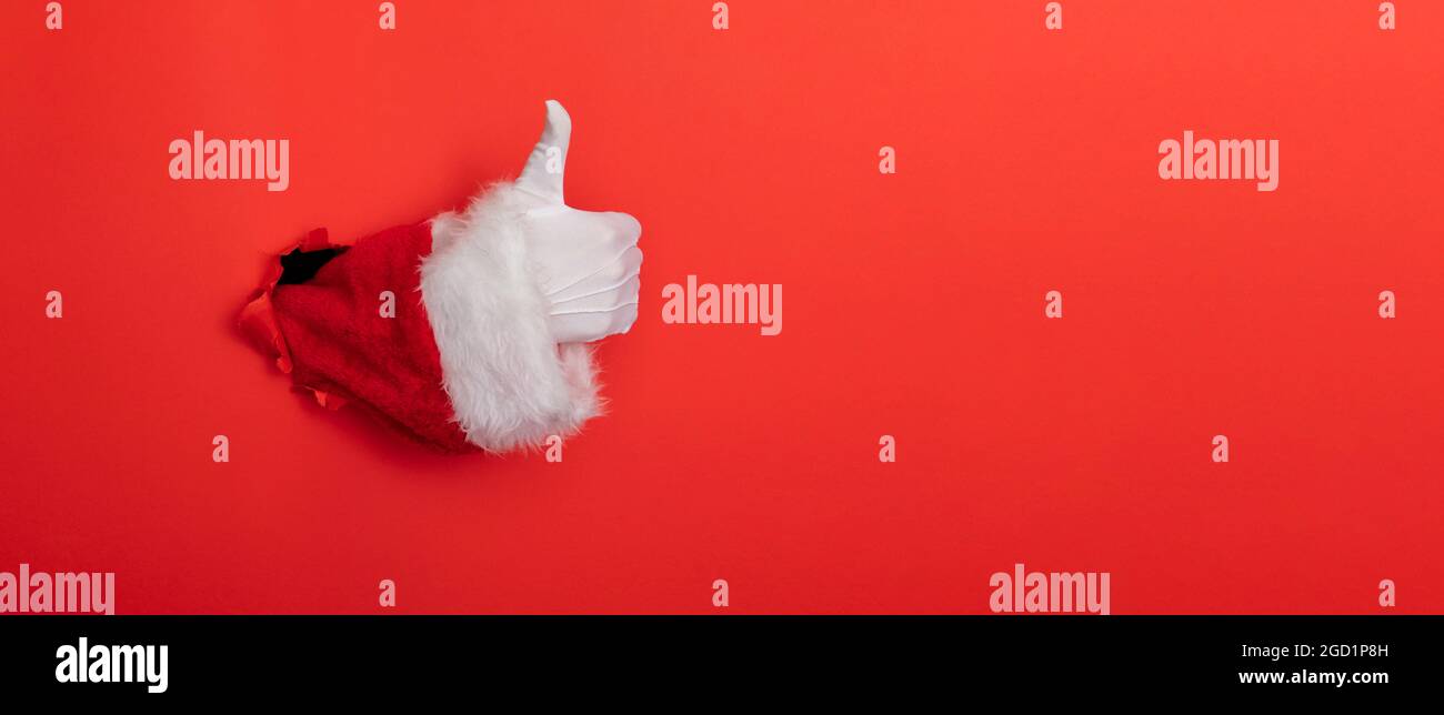 Babbo Natale mano pollici su attraverso un buco in carta sfondo rosso Foto Stock