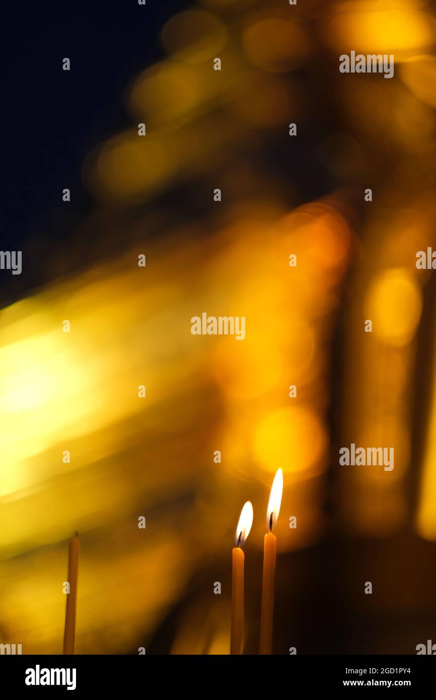 Due candele accese e una bruciata contro uno sfondo dorato astratto in un tempio buddista in Thailandia Foto Stock